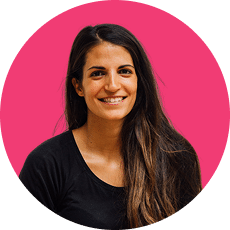 A person with long dark hair, wearing a black shirt, smiles against a bright pink circular background.